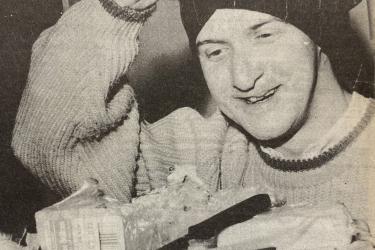 Man lifting off his mask after cheese-tasting and holding a cheese board at the Greenwich Lesbian and Gay Centre's gay men's group event, November 1988