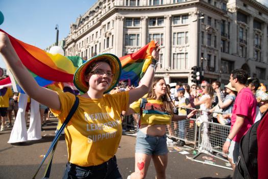 A young person holding a rainbow flag and wearing a yellow METRO t-shirt at Pride in London