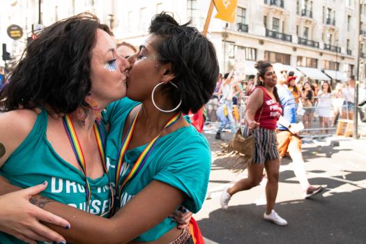 Two people wearing METRO green t-shirts and kissing at Pride in London