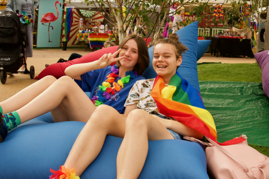 Two young people, one wearing a rainbow flag, sitting on a blue METRO beanbag