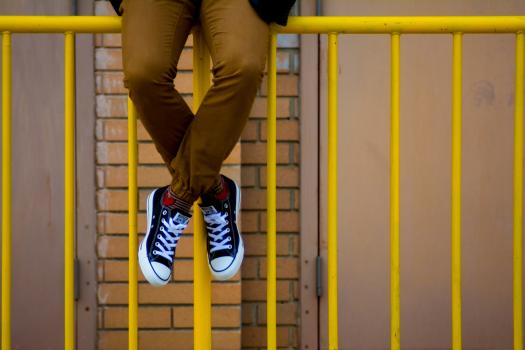 A young man sitting on yellow railings wearing sneakers