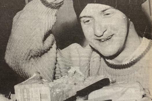 Man lifting off his mask after cheese-tasting and holding a cheese board at the Greenwich Lesbian and Gay Centre's gay men's group event, November 1988