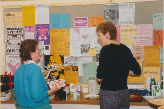 Two people talking in front of the Greenwich Lesbian and Gay Centre community information noticeboard in 1986