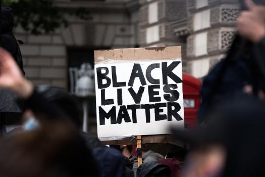 Photo focused on placard saying 'Black Lives Matter' in protesting crowd by red phone box by Whitehall