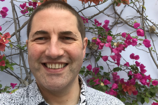 Photo of Simon with flowers growing up a wall behind him