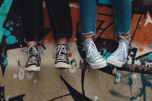 Photo of legs and converse of teenagers in front of a graffitied wall