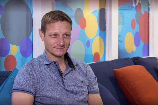 Headshot of photo of Andrew in front of windows with a multi-coloured bubble design on